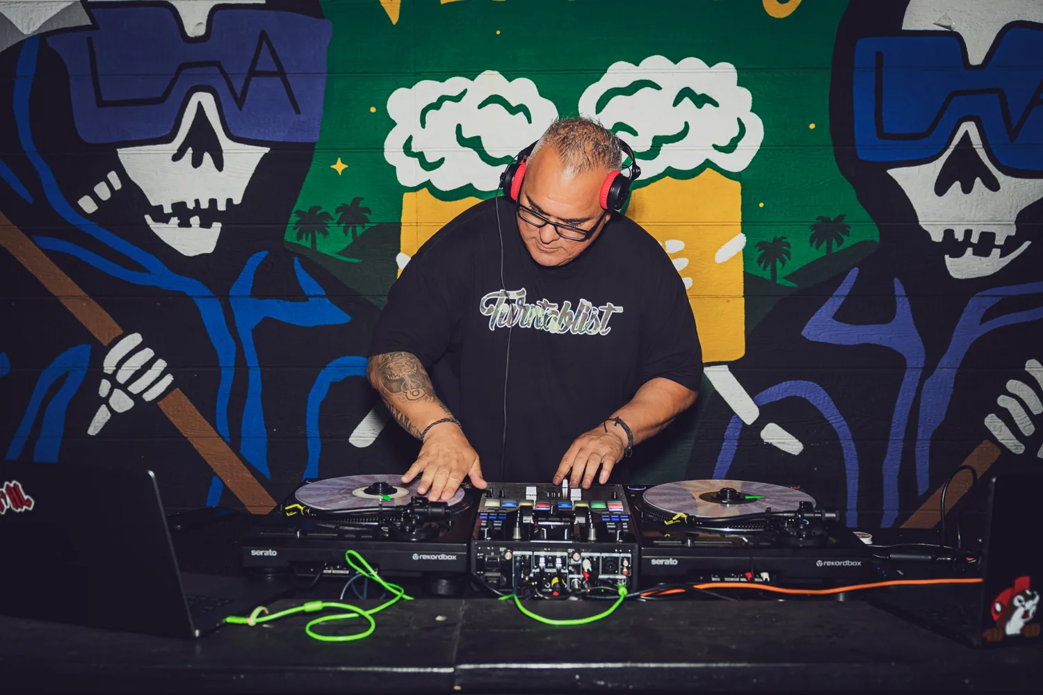 DJ Big Al performing at Verdugo Bar with colorful artwork behind him