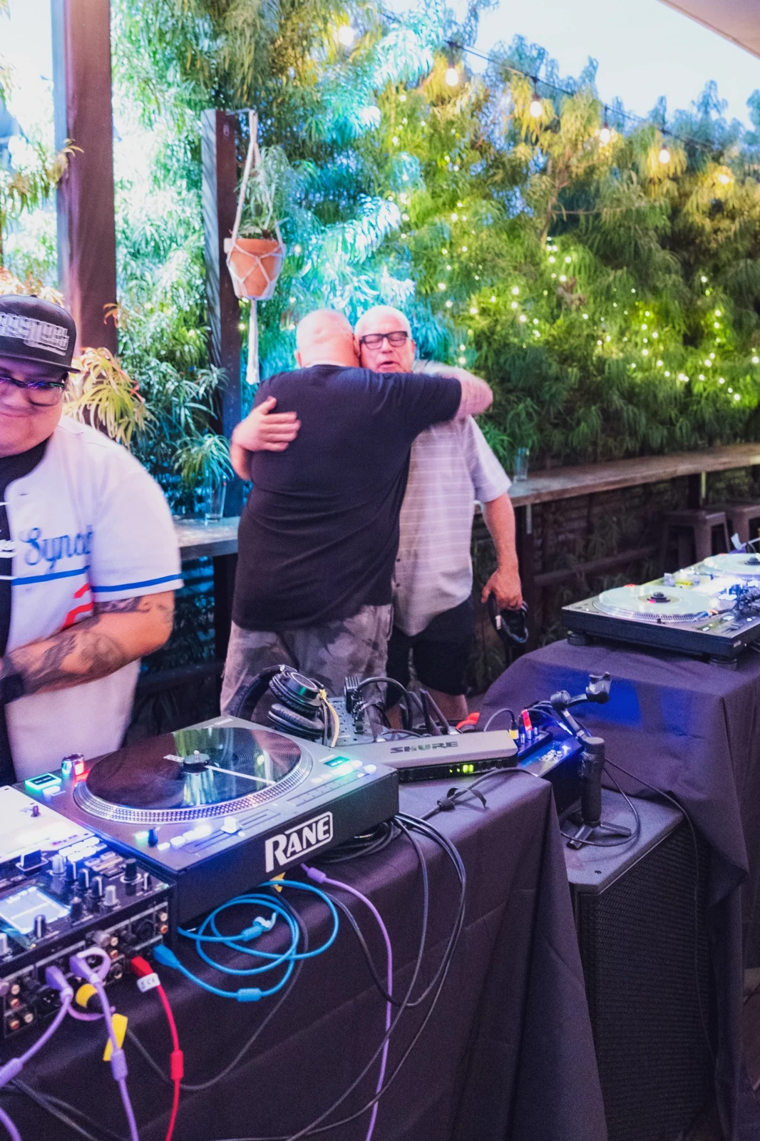 DJ Big Al embracing DJ Tony G beside the turntables